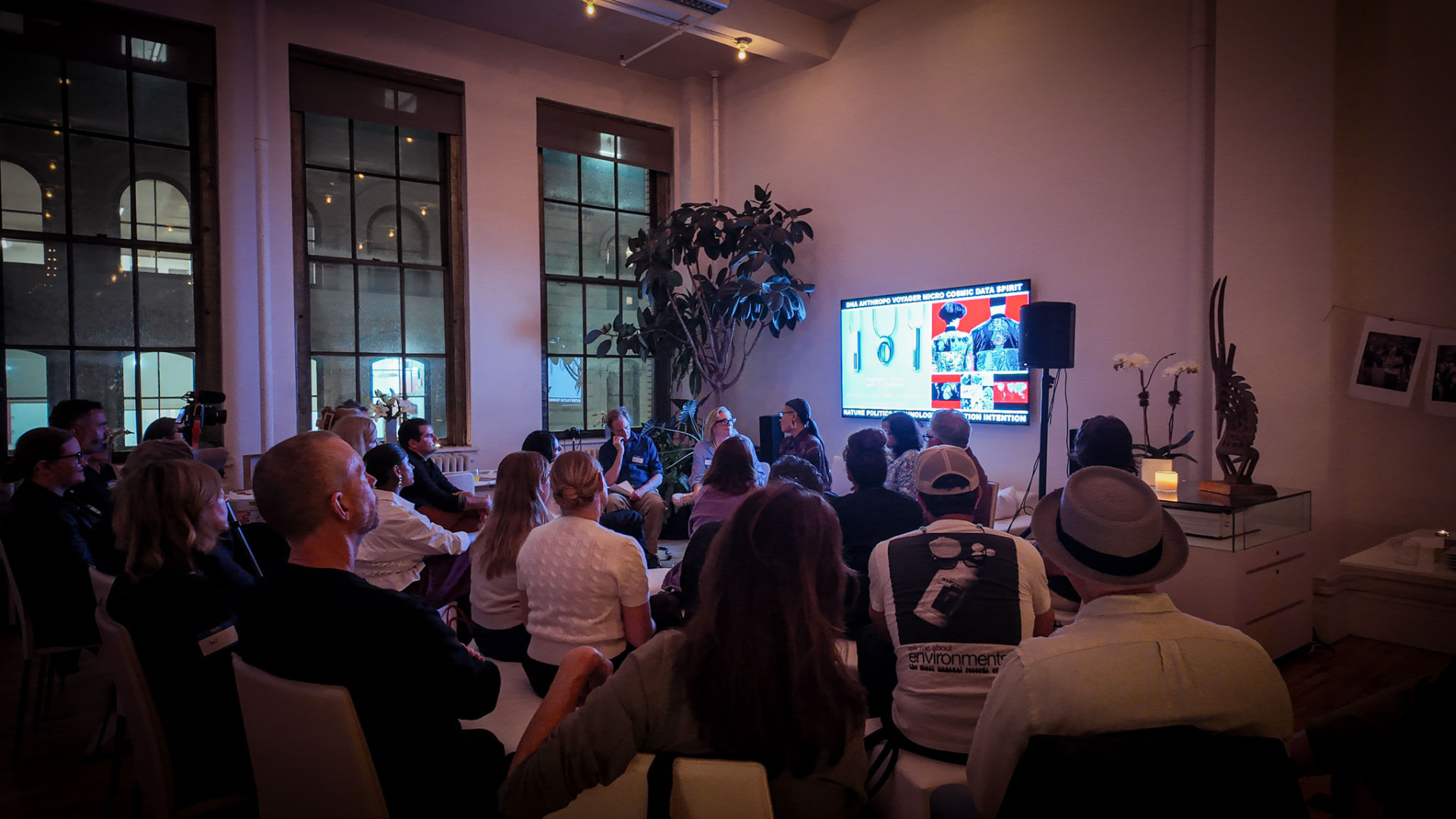 An audience with their backs to us, watching a panel